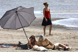Two woman relaxing under a large sunshade on a sunny beach, Pärnu, Estonia