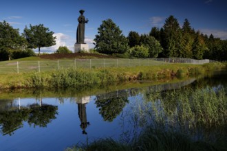 Socialist statue in Grutas Park is reflected in a calm body of water surrounded by trees,