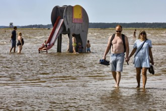 Couple walking in shallow water on a beach near an elephant water slide, Pärnu, null, Estonia