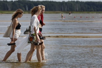 Three woman walking in the shallow water of a beach surrounded by vast nature, Pärnu, zero, Estonia