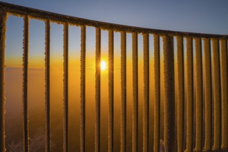 Sunset behind an icy railing with orange sky in the Teutoburg Forest on the Steinegge observation