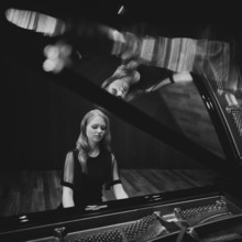 Young woman, pianist, in evening dress playing on an unfolded Steinway & Sons grand piano, black