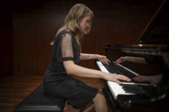 Young woman, pianist, side view playing on a Steinway & Sons grand piano in evening dress,