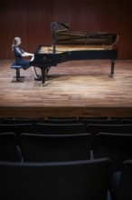 Young woman, pianist, in evening dress, in a concert hall, playing on a Steinway & Sons grand