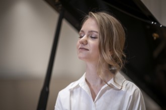 Dreamy looking young woman, pianist, wearing white blouse in front of Steinway & Sons grand piano,
