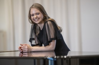 Laughing young woman, pianist, in evening dress leaning on a Steinway & Sons grand piano,
