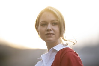 Self-confidently looking young woman in white blouse and red cardigan, in backlight, Stuttgart,