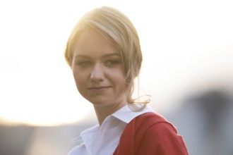 Serious looking young woman in white blouse and red cardigan, in backlight, Stuttgart,