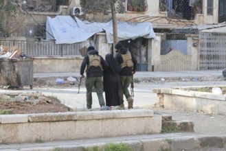In Aleppo, Syria on January 10, 2026, Syrian Army soldiers assist and secure an elderly woman