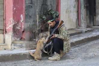 In Aleppo, Syria on January 10, 2026, a Syrian Army soldier crouches to pet a stray cat in the