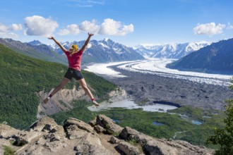 Young woman jumping into the air, view of impressive mountain landscape with Matanuska glacier and