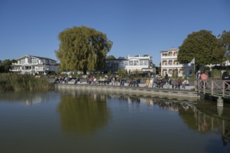 Tourists sunbathe on the promenade of Schmachter See, in the back buildings of spa architecture,