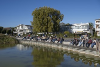 Tourists sunbathe on the promenade, Schmachter See, spa architecture buildings in the back, Binz,