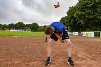 A boy on a sports field throws a rubber boot into the air with effort, sports and fun Olympics