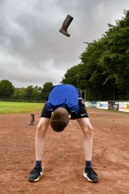 A boy throws a rubber boot high in the air on a sports field rubber boot long throw, sports and fun
