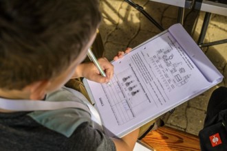 Child concentrates on a worksheet while writing, table and sunlight in the background, event for