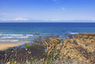 Rocky seashore in low tide with rolling sea waves and a seascape view to the horizon on a sunny
