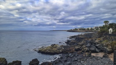 Rocky coast overlooking the sea and urban buildings under a cloudy sky, Playa Blanca Lanzarote