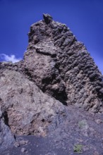 View of a high volcanic rock structure under a clear blue sky, partial view of El Cuervo volcano,