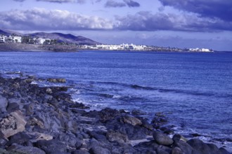 Rocky coastal landscape with views of the sea and a distant town under a cloudy sky, Playa Blanca