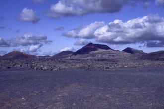 View of a vast volcanic landscape with colorful mountains under a cloudy sky, Tinajo Lanzarote