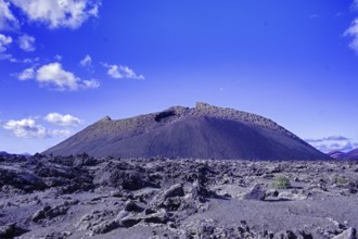 The El Cuervo volcano (Caldera de los Cuervos) rises above a lava field under a clear blue sky,