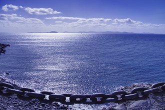 Chain on the edge of a cliff with a view of a calm, blue sea and distant island of Furteventura in
