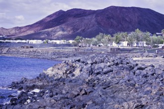 Rugged coastal area with rocks and views of reddish brown mountains under cloudy sky, Playa Blanca