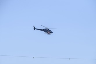A helicopter flies over a high-voltage line in the air during technical work, Lemförde, Lower