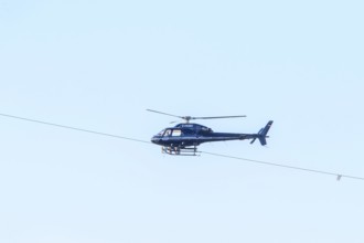 A blue helicopter flies in a clear sky. Technical details are visible, marking work on a new