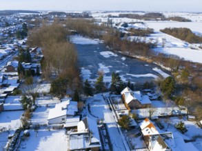 Winter village scene with snow-covered houses and a frozen lake in a quiet landscape, aerial view,