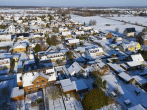 Snow-covered residential area with various houses and roads surrounded by fields, aerial view,