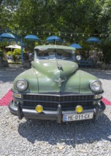 Front view of a green vintage car on a red carpet surrounded by umbrellas and pebbles, vintage car,