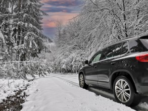 Black SUV driving on deep snowy road through winter forest, Baden-Württemberg, Germany