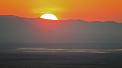 Sunrise with red fireball of rising sun over mountain ridges and extensive steppe landscape in the