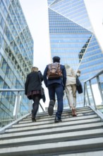 Diverse business colleagues climb a modern exterior staircase against glass skyscrapers,