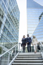 Diverse business professionals in formal attire walking down modern city stairs between glass
