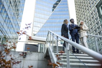 Diverse business professionals smiling and interacting while looking at a tablet on modern outdoor