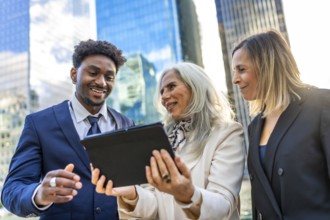 Diverse business professionals reviewing information on a digital tablet, standing outdoors in