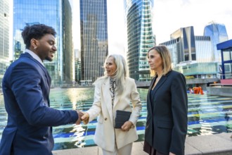 Diverse business professionals, a black man and two women, are shaking hands and discussing in a