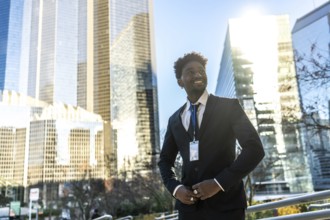 Young african american businessman in a dark suit and id badge smiles confidently in a sunny urban