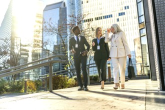 Three diverse business colleagues with name badges walking outdoors in a modern city discussing