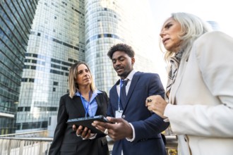 Diverse business professionals collaborating on a digital tablet, standing outdoors in front of