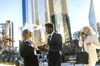 Diverse business professionals engaging in an outdoor meeting, sharing information on a tablet, and