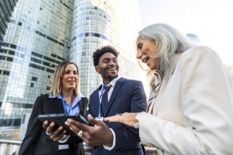 Diverse business professionals smiling and interacting, using a digital tablet for outdoor