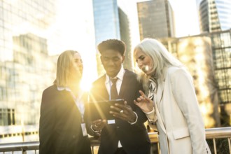 Diverse multi generation business team outdoors at sunset, collaborating over a digital tablet amid