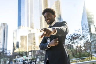 Young black businessman smiling and pointing directly towards the viewer with one hand, standing