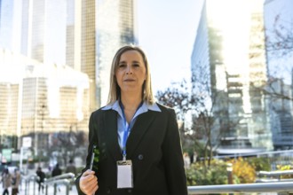 Professional businesswoman standing outdoors in a modern downtown area, wearing a suit and lanyard