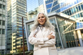Senior businesswoman with gray hair and a formal elegant blazer standing outdoors with folded arms,