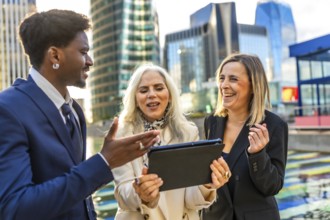 Diverse business professionals having an animated outdoor meeting, looking at a digital tablet and